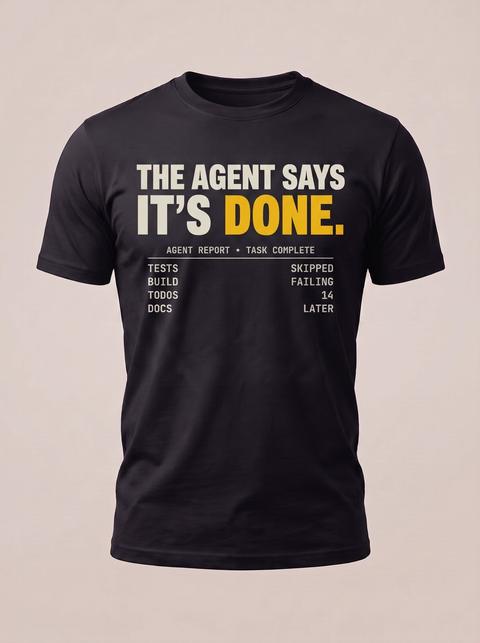 It Says It's Done tee in Black. Fitted mockup. Printed: THE AGENT SAYS / IT’S DONE. / AGENT REPORT · TASK COMPLETE / TESTS / SKIPPED / BUILD / FAILING / TODOS / 14 / DOCS / LATER.